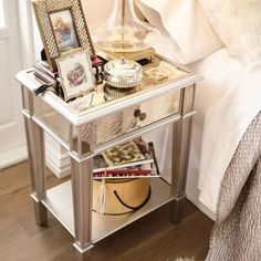 a mirrored nightstand with pictures and other items on it in front of a white bed