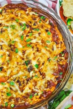 a casserole dish with cheese and vegetables in it on a table next to tortilla chips