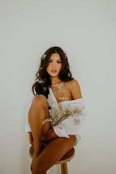 a beautiful woman sitting on top of a stool holding a bouquet of flowers in her hand