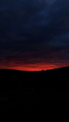 the sky is dark and red as the sun sets in the distance with clouds above it