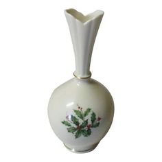 a white vase with holly and berries painted on the front, sitting against a white background