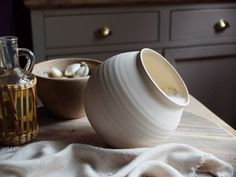 a white vase sitting on top of a wooden table next to a bottle and bowl