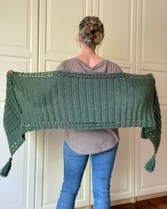 a woman standing in front of a white wall holding up a green knitted blanket