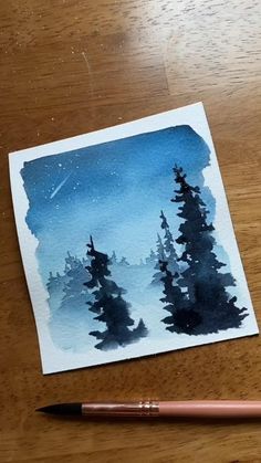 a watercolor painting of some trees on a wooden table with a pen and paper