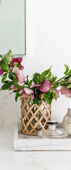 pink flowers in a wicker basket on a marble countertop next to a bottle of body lotion