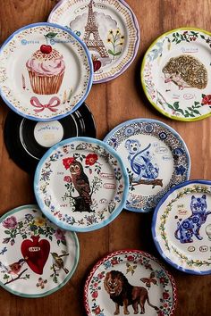 many plates with different designs on them sitting on a wooden table next to each other