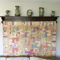 a quilted wall hanging above a bed with pillows and vases on the headboard