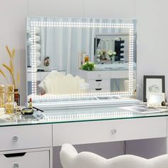 a dressing table with a lighted mirror and stool in front of it, next to a white chair