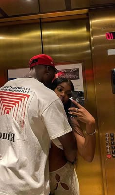 a man and woman standing in front of an elevator looking at their cell phones together