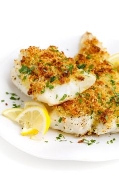 two pieces of fish on a white plate with lemon wedges and parmesan cheese