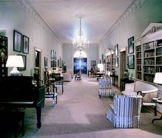 a long hallway with many chairs and lamps on either side of the room, leading to an open door