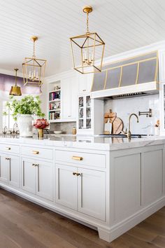 a kitchen with white cabinets and gold hardware on the handles, brass fixtures and hanging lights