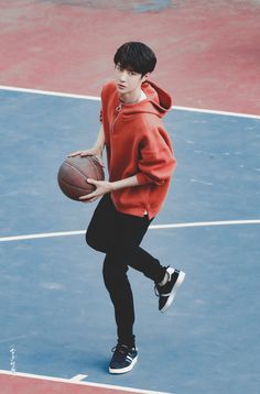 a young man holding a basketball on top of a tennis court with a ball in his hand