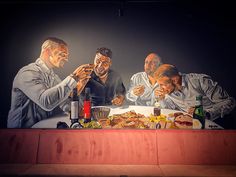 three men sitting at a table with food in front of them and one man eating