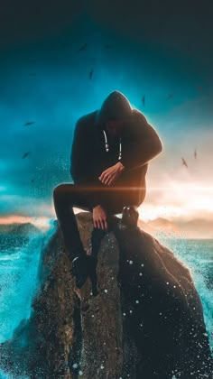 a man sitting on top of a rock in the ocean with birds flying around him