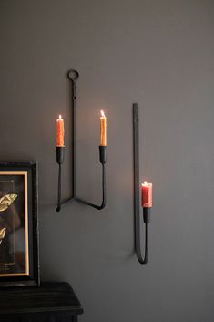 three candles are lit on the wall next to a framed painting and two sconces