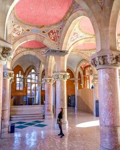 a woman is standing in the middle of a large building with columns and arches on both sides