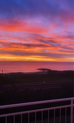 the sun is setting over the ocean and it's colors are pink, blue, yellow, and orange