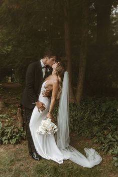 a bride and groom kissing in front of some trees at their wedding day, black and white photo