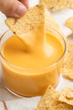 a person dipping some crackers into a small glass bowl filled with orange liquid and cheese