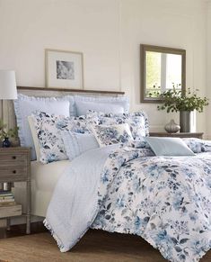 a bed with blue and white comforters in a room next to a dresser, mirror and lamp