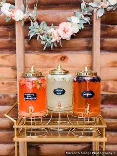 three jars filled with liquid sitting on top of a metal stand next to flowers and greenery