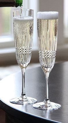 two champagne flutes are being filled with sparkling liquid on a table next to a window