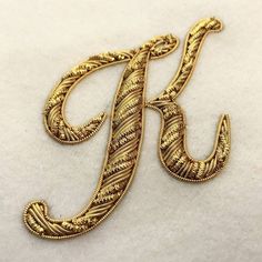 the letter k is made out of gold wire and has an intricate design on it