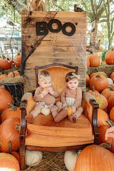 two young children sitting on an old fashioned chair in front of pumpkins and hay