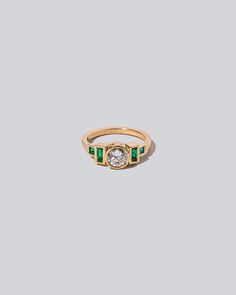 a gold ring with green and white stones on the sides, set against a gray background