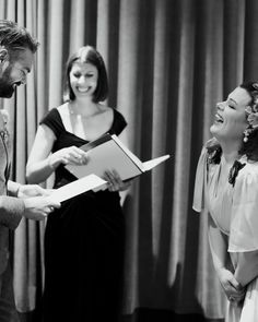 two women and a man are laughing while one woman is holding a piece of paper