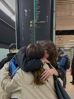 two people hugging each other in front of a subway sign with directions to the trains