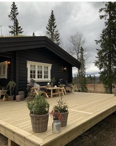 a wooden deck with potted plants on it and a black cabin in the background