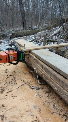 an orange and black chainsaw sitting on top of a piece of wood in the woods