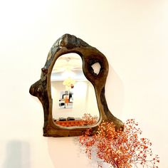 a mirror hanging on the wall next to a vase with flowers in it and an orange plant