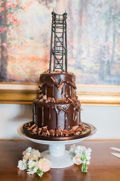 a chocolate cake sitting on top of a wooden table next to flowers and a painting