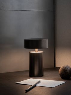 a black lamp sitting on top of a wooden table next to a pen and paper