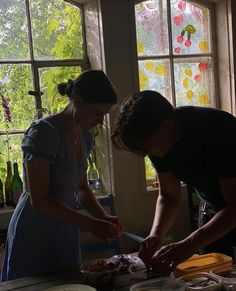 two people standing in front of a window cutting food on a table with utensils