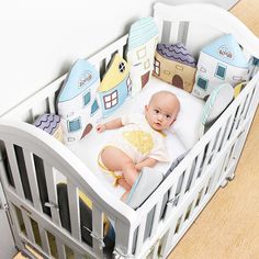 a baby laying in a crib with pillows on it's sides and houses