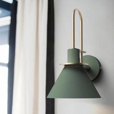 a green wall light mounted on the side of a white wall next to a window