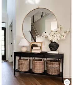 a black console table with baskets and flowers on it in front of a large round mirror