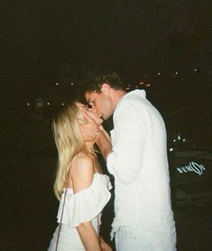 a man kissing a woman on the cheek in front of a dark sky at night