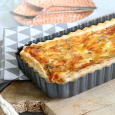 a quiche dish sitting on top of a cutting board next to a knife and fork