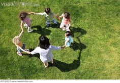 a group of children holding hands in the shape of a heart on green grass, overhead view from above