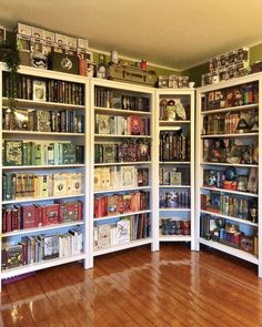 a room filled with lots of books on top of white bookcases next to a wooden floor