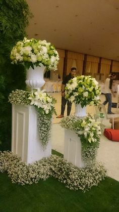 three tall white vases with flowers are on display in front of a man and woman