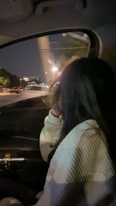 a woman sitting in the passenger seat of a car driving down a street at night