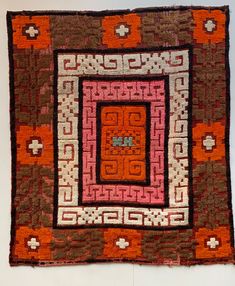 an orange, brown and pink rug with squares on the center is hanging on a wall