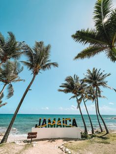 there is a sign that says jamaica on the beach with palm trees in front of it