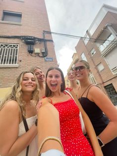 four young women taking a selfie in front of a brick building on a city street